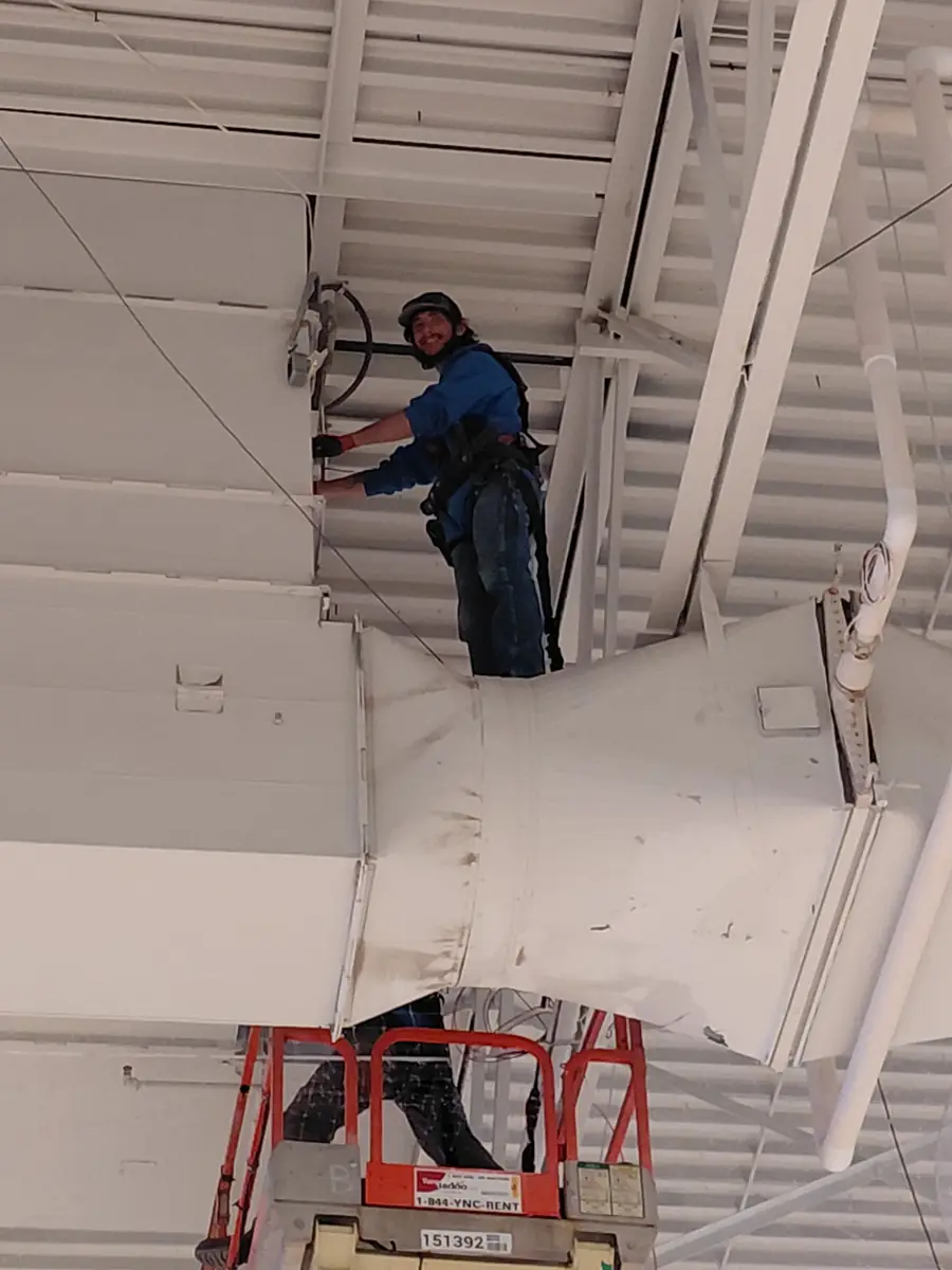 Electrician on a scissor lift working on overhead equipment in a commercial building