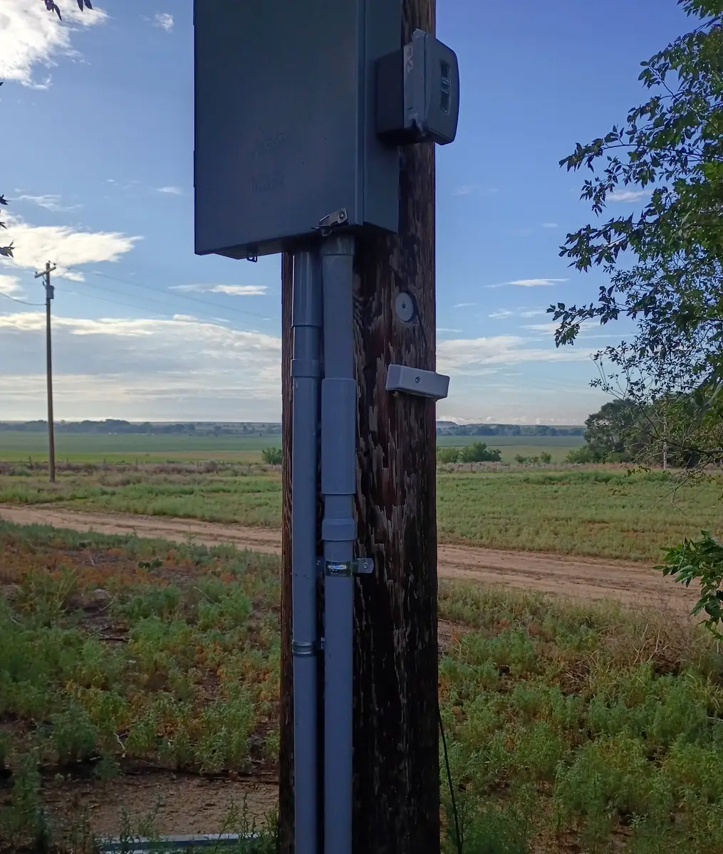 Service panel and conduit on a wooden pole beside irrigated farm fields in Otero County